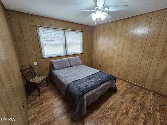 bedroom featuring wood walls, dark wood finished floors, and a ceiling fan