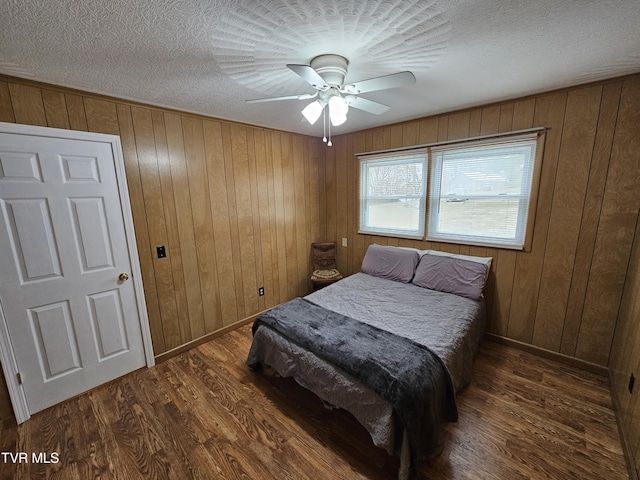 bedroom featuring ceiling fan, a textured ceiling, wooden walls, baseboards, and dark wood-style floors