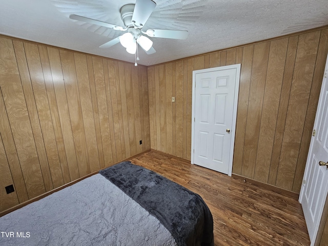 bedroom with ceiling fan, wood walls, a textured ceiling, and wood finished floors