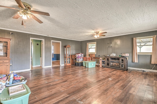 interior space featuring a ceiling fan, a textured ceiling, ornamental molding, and wood finished floors