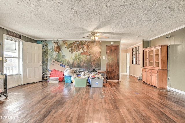 unfurnished living room featuring a textured ceiling, ceiling fan, wood finished floors, baseboards, and crown molding