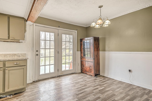 doorway to outside featuring baseboards, a textured ceiling, light wood-style floors, a chandelier, and beam ceiling