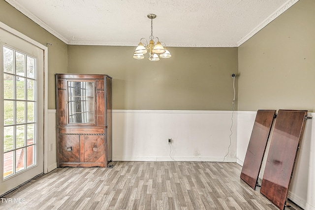 unfurnished dining area featuring an inviting chandelier, a textured ceiling, ornamental molding, and wood finished floors