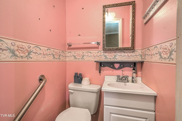 half bath with toilet, a wainscoted wall, and vanity