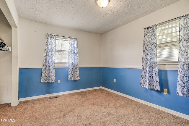 empty room with carpet, visible vents, and a textured ceiling