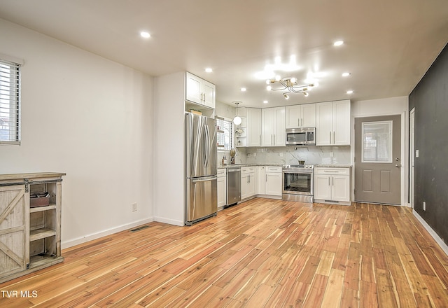 kitchen featuring stainless steel appliances, baseboards, light wood-style floors, white cabinets, and backsplash