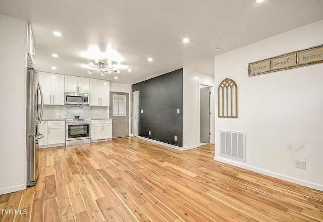 kitchen featuring light wood finished floors, visible vents, white cabinets, decorative backsplash, and stainless steel appliances