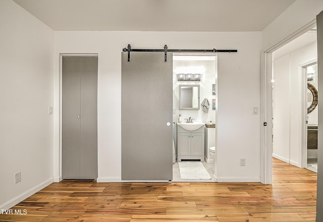 unfurnished bedroom with a barn door, a sink, light wood-style flooring, and baseboards