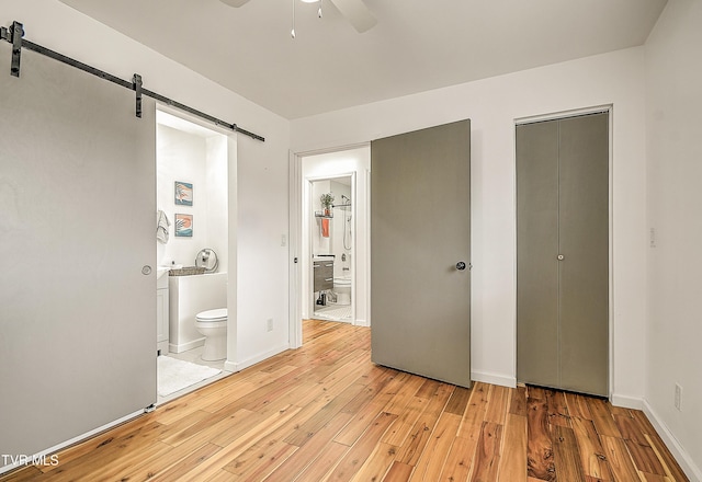 unfurnished bedroom featuring light wood-style floors, connected bathroom, baseboards, and a barn door