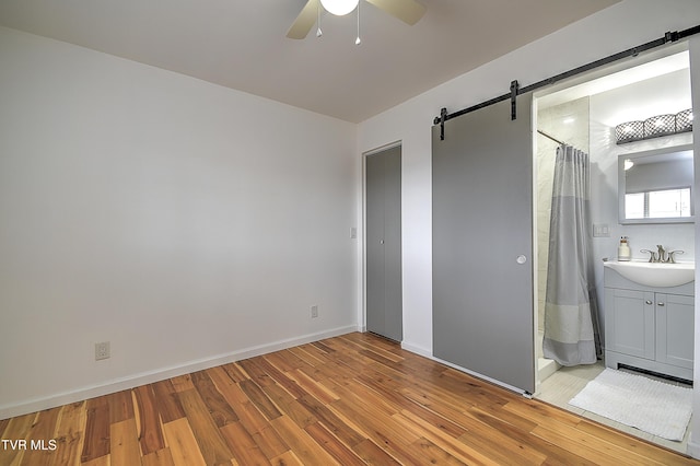 unfurnished bedroom featuring ceiling fan, a barn door, a sink, baseboards, and light wood-type flooring