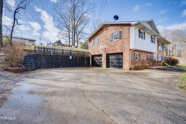 view of side of home featuring a garage, fence, concrete driveway, and brick siding