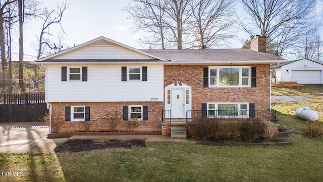 bi-level home with a chimney, a front lawn, an outbuilding, and brick siding