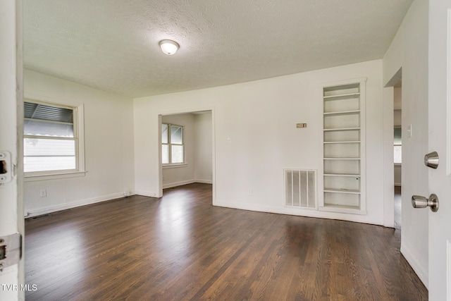 unfurnished room with built in shelves, baseboards, visible vents, dark wood-style flooring, and a textured ceiling