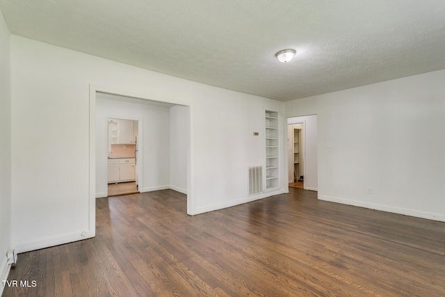 spare room featuring dark wood finished floors, visible vents, a textured ceiling, and baseboards