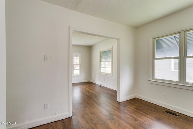 unfurnished room with dark wood-style floors, visible vents, a textured ceiling, and baseboards