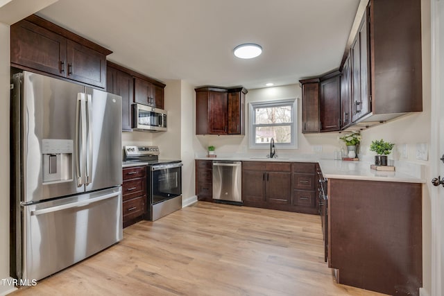 kitchen featuring dark brown cabinetry, light wood finished floors, appliances with stainless steel finishes, and a sink