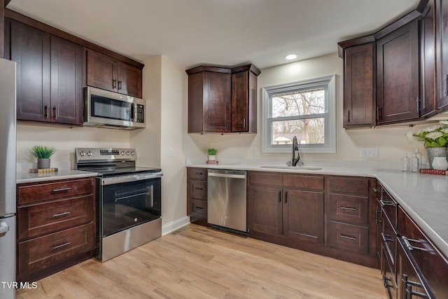 kitchen featuring light wood-style flooring, a sink, light countertops, dark brown cabinetry, and appliances with stainless steel finishes