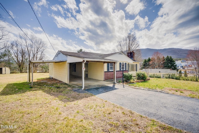 view of front of home with brick siding, a mountain view, a carport, driveway, and a front lawn