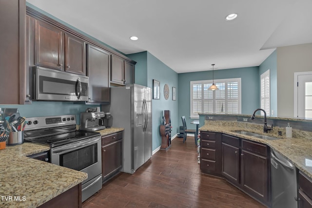 kitchen featuring dark brown cabinetry, light stone counters, appliances with stainless steel finishes, dark wood-type flooring, and a sink