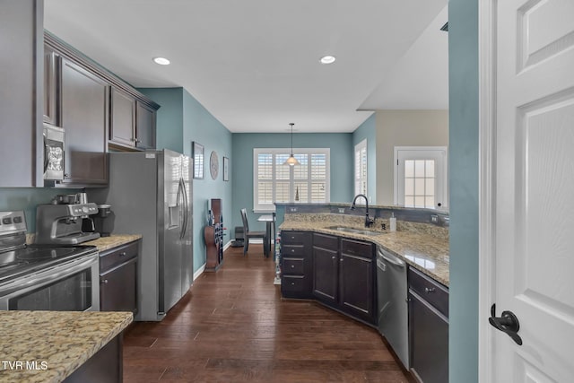 kitchen featuring light stone counters, dark wood-style floors, appliances with stainless steel finishes, a sink, and a peninsula