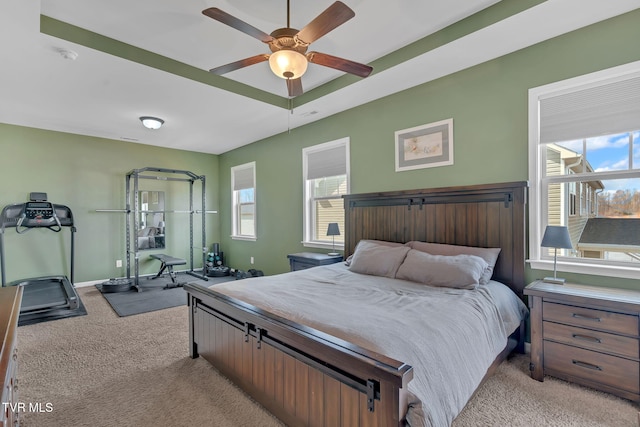 bedroom with ceiling fan, multiple windows, a raised ceiling, and light colored carpet