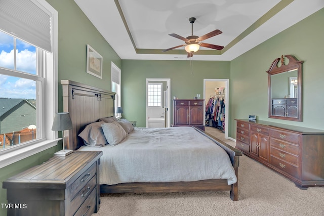 bedroom with light colored carpet, a ceiling fan, a spacious closet, a closet, and a raised ceiling