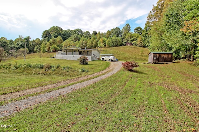 view of front of house with driveway, an outbuilding, a storage unit, a wooded view, and a front yard