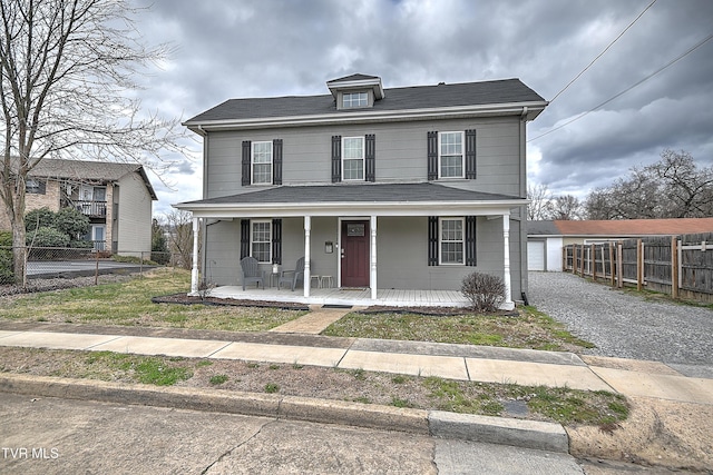 american foursquare style home featuring covered porch, driveway, an outdoor structure, and fence