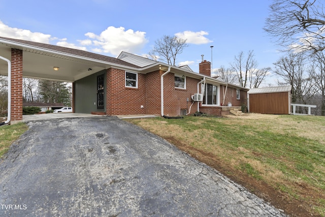 view of front of property with aphalt driveway, brick siding, a carport, a front lawn, and a chimney