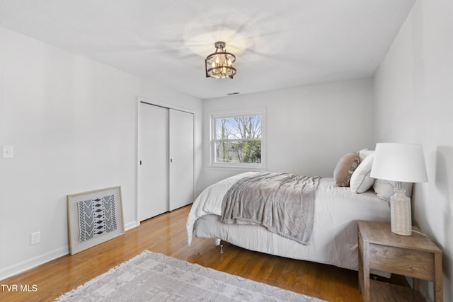 bedroom with a closet, baseboards, visible vents, wood finished floors, and a notable chandelier