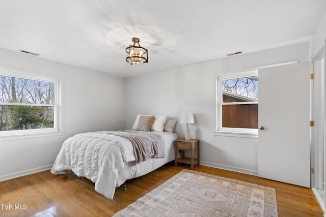 bedroom with an inviting chandelier, visible vents, baseboards, and wood finished floors