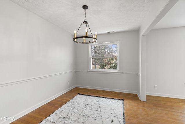 dining area with visible vents, an inviting chandelier, a textured ceiling, wood finished floors, and baseboards