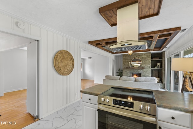 kitchen featuring dark countertops, stainless steel electric range oven, island exhaust hood, and a fireplace