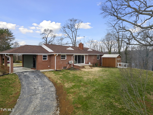 rear view of property with a chimney, aphalt driveway, an outbuilding, a storage unit, and brick siding