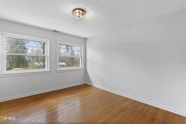 empty room featuring wood finished floors, visible vents, and baseboards