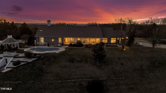 back of house at dusk with a lawn and a gazebo