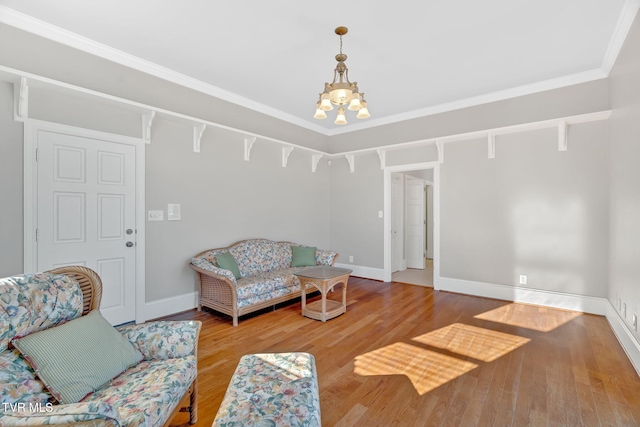 living room with baseboards, a notable chandelier, ornamental molding, and wood finished floors