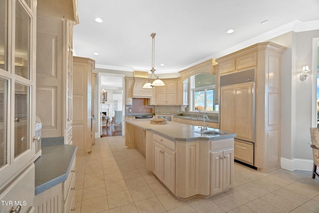 kitchen featuring a center island with sink, ornamental molding, paneled built in refrigerator, light brown cabinetry, and a sink