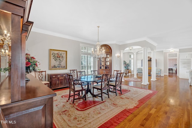 dining room with arched walkways, crown molding, light wood finished floors, an inviting chandelier, and ornate columns