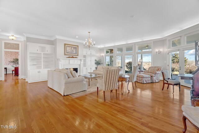 living area with light wood-style floors, a lit fireplace, crown molding, and an inviting chandelier