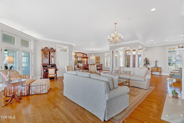 living room featuring arched walkways, crown molding, light wood-style floors, a chandelier, and ornate columns