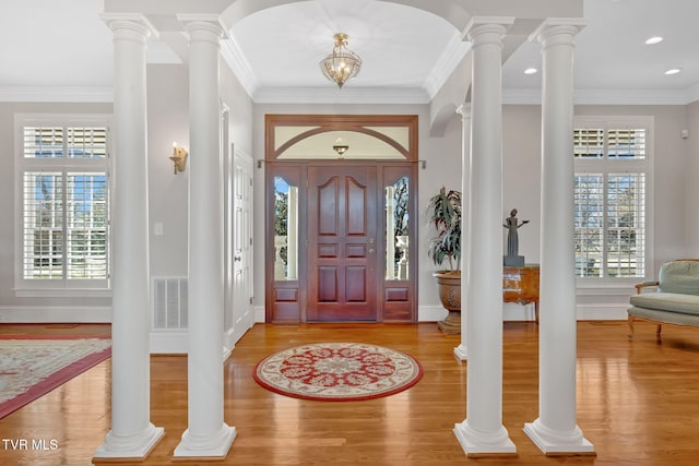 foyer with wood finished floors, visible vents, baseboards, ornamental molding, and decorative columns