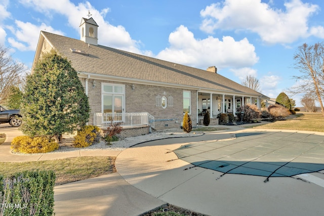 rear view of house featuring a shingled roof, a chimney, covered porch, a patio area, and brick siding