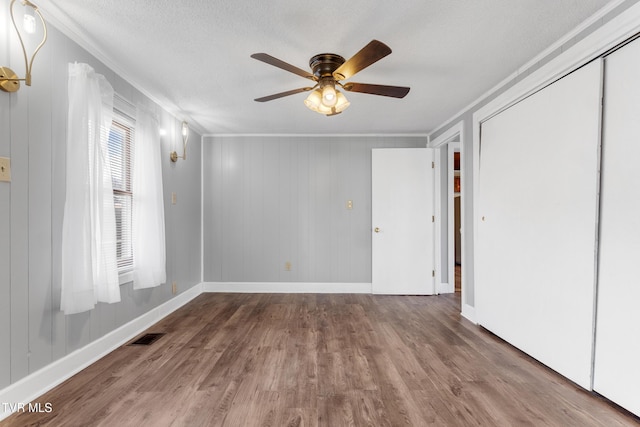 empty room with a textured ceiling, wood finished floors, visible vents, baseboards, and ornamental molding