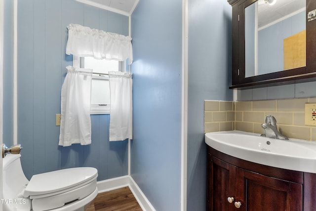 half bathroom featuring decorative backsplash, toilet, ornamental molding, wood finished floors, and vanity