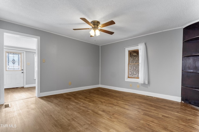 unfurnished room featuring a textured ceiling, wood finished floors, visible vents, and crown molding