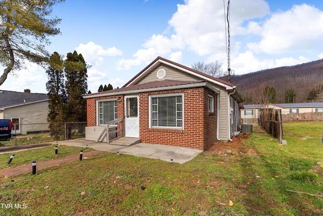 bungalow with central AC unit, a patio, fence, a front lawn, and brick siding