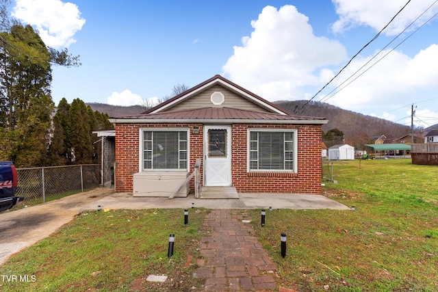 bungalow-style house featuring brick siding, metal roof, fence, a mountain view, and a front lawn