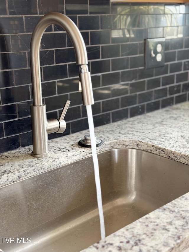 interior details with a sink, light stone countertops, and tasteful backsplash