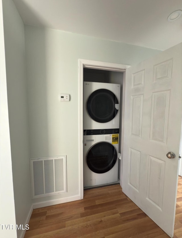 laundry room with visible vents, stacked washer and clothes dryer, wood finished floors, baseboards, and laundry area